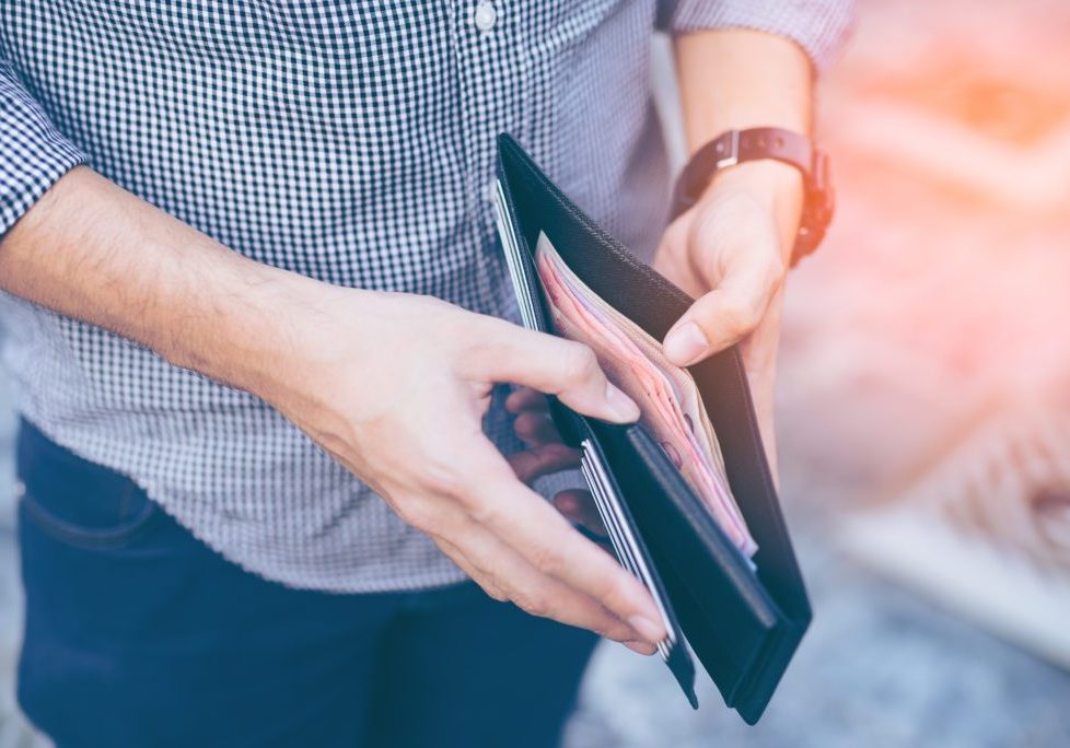 Man standing holding black wallet full of money